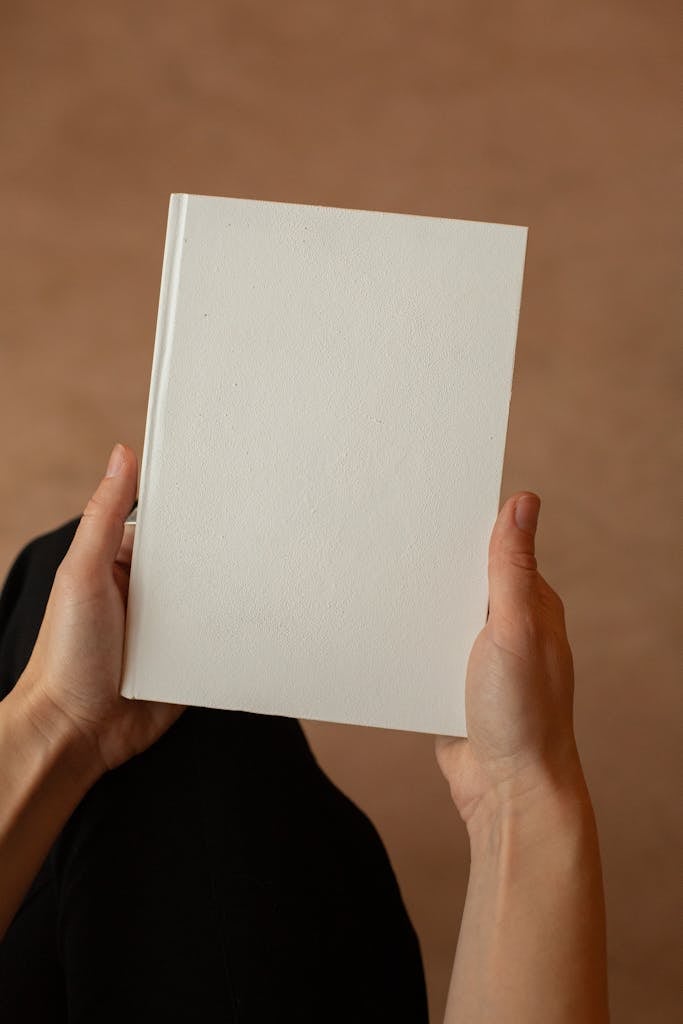 Crop faceless person in studio with white sheet of paper sitting in light room